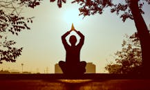 Silhouette of a person practicing yoga outdoors during sunrise, creating a calming atmosphere.